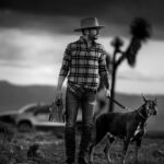 Black and white photo of man with hat and dog in Guanajuato's dramatic landscape.